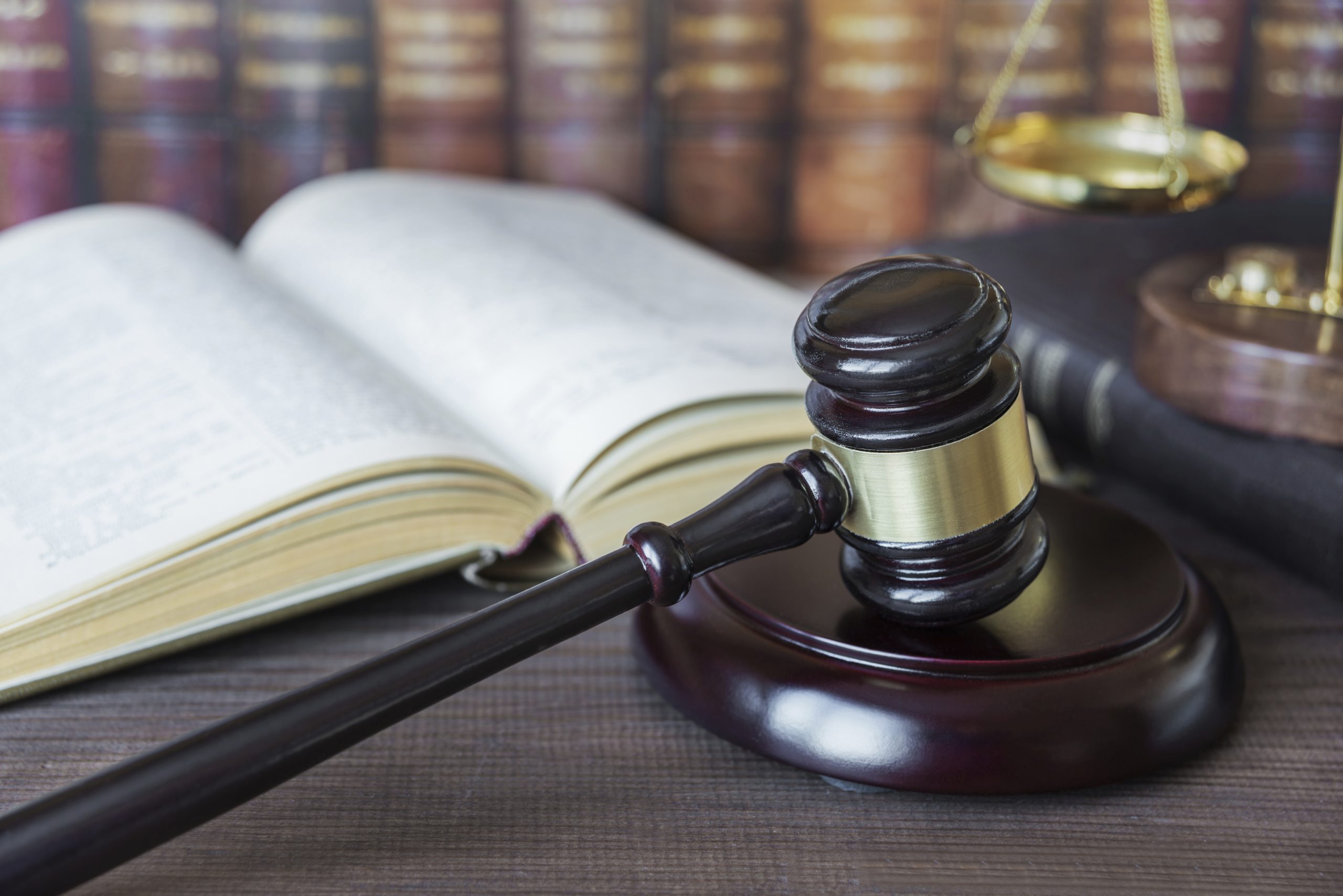 Wood gavel, soundblock, scales and opened old book against the background of a row of antique books bound in leather